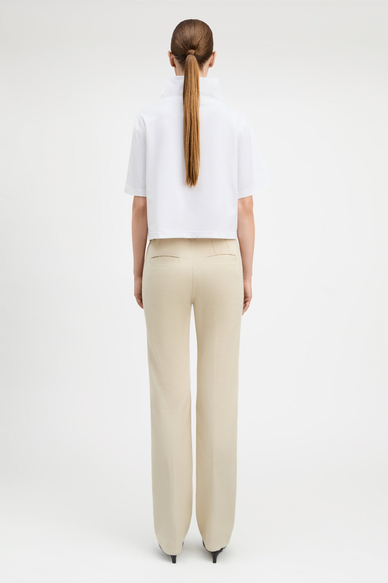 Woman wearing straight cut parchment color jeans with white top, back view.