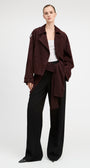 A model stands against a light gray studio background wearing a dark burgundy corduroy jacket over a white top and black wide-leg trousers.