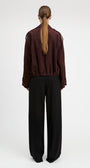 A model shown from the back wearing a dark burgundy cropped jacket with shoulder epaulets and black wide-leg trousers, set against a plain light gray studio background.