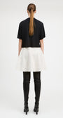 A model shown from the back wearing a black short-sleeve cropped top, a fluffy white mini skirt, black leather-look over-the-knee boots, and black high heels against a plain white studio background.