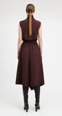 A woman viewed from the back wearing a sleeveless high-neck midi dress in deep burgundy, paired with black heeled boots, against a plain light gray studio background.