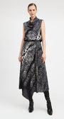 A model wears a sleeveless black and white abstract patterned midi dress with a high cowl neck, a matching black belt, and black knee-high boots, photographed against a light gray studio background.