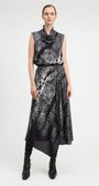 A model stands against a light gray studio background wearing a sleeveless, high-neck midi dress with an abstract black and white pattern and black pointed boots.