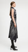 A woman in profile wearing a sleeveless black midi dress with a white abstract pattern, paired with black knee-high boots, against a plain light gray studio background.