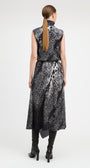 A woman viewed from the back wearing a sleeveless high-neck midi dress with a black and white abstract pattern, paired with black knee-high boots, against a light gray studio background.