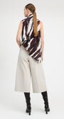 A woman is shown from the back wearing a sleeveless top with a black, white, and dark red abstract brushstroke pattern, paired with light beige wide-leg cropped pants and black knee-high boots, against a plain white studio background.
