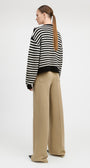 A woman shown from the back wearing a black and white striped knit sweater and beige wide-leg trousers, standing against a light gray studio background.