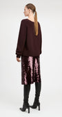 A woman shown from the back wearing a dark burgundy knit sweater, a pink sequined midi skirt, black over-the-knee boots, and black ankle boots, against a plain light gray studio background.