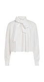 A white long-sleeve blouse with a high collar and a large bow tied at the front, shown against a plain white background.